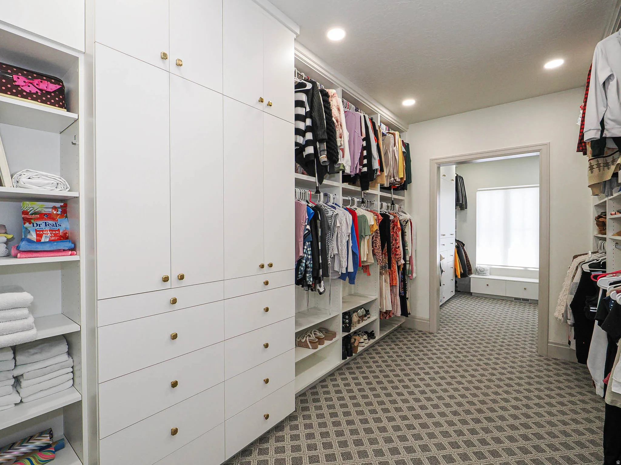 Custom closet system featuring white cabinetry, brass-toned hardware, recessed lighting, and patterned carpeting