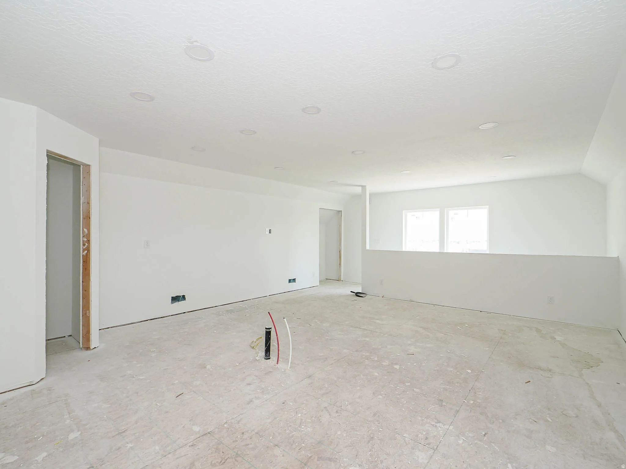 Expansive open-concept room featuring a half-wall partition, multiple recessed ceiling lights, and multiple windows providing natural light