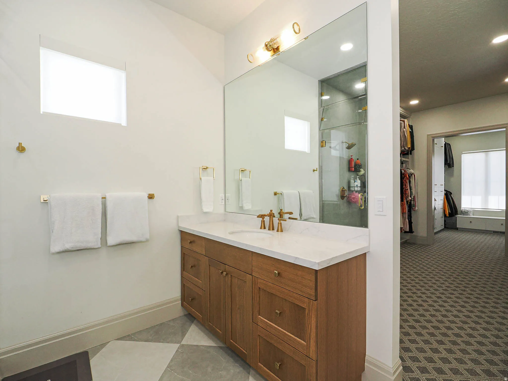 Bathroom vanity featuring a light wood-finish cabinet with brass hardware, a white countertop, and a large wall-mounted mirror