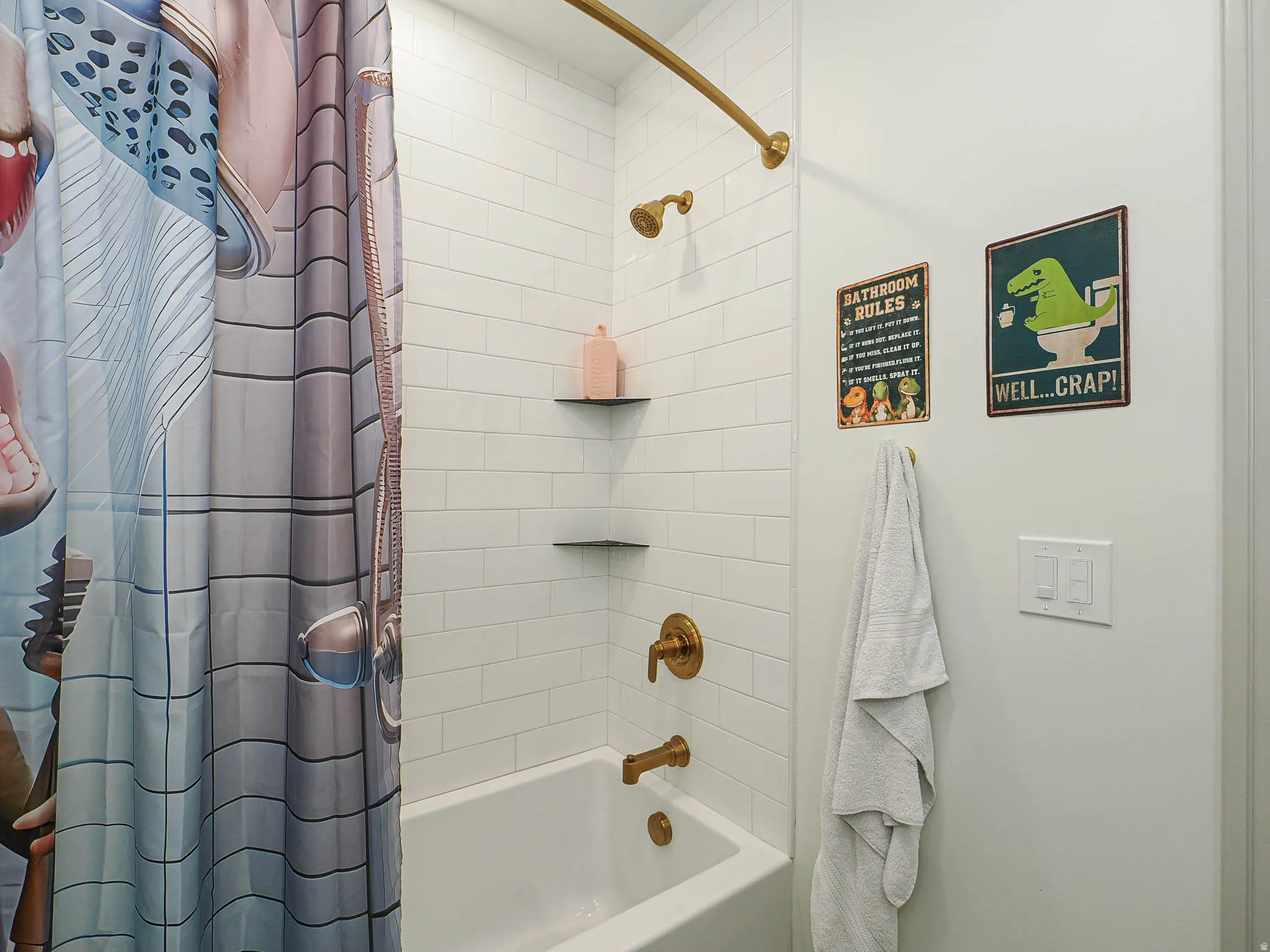Bathtub shower combination featuring white subway tile surround, brass-finish fixtures, and built-in corner shelving