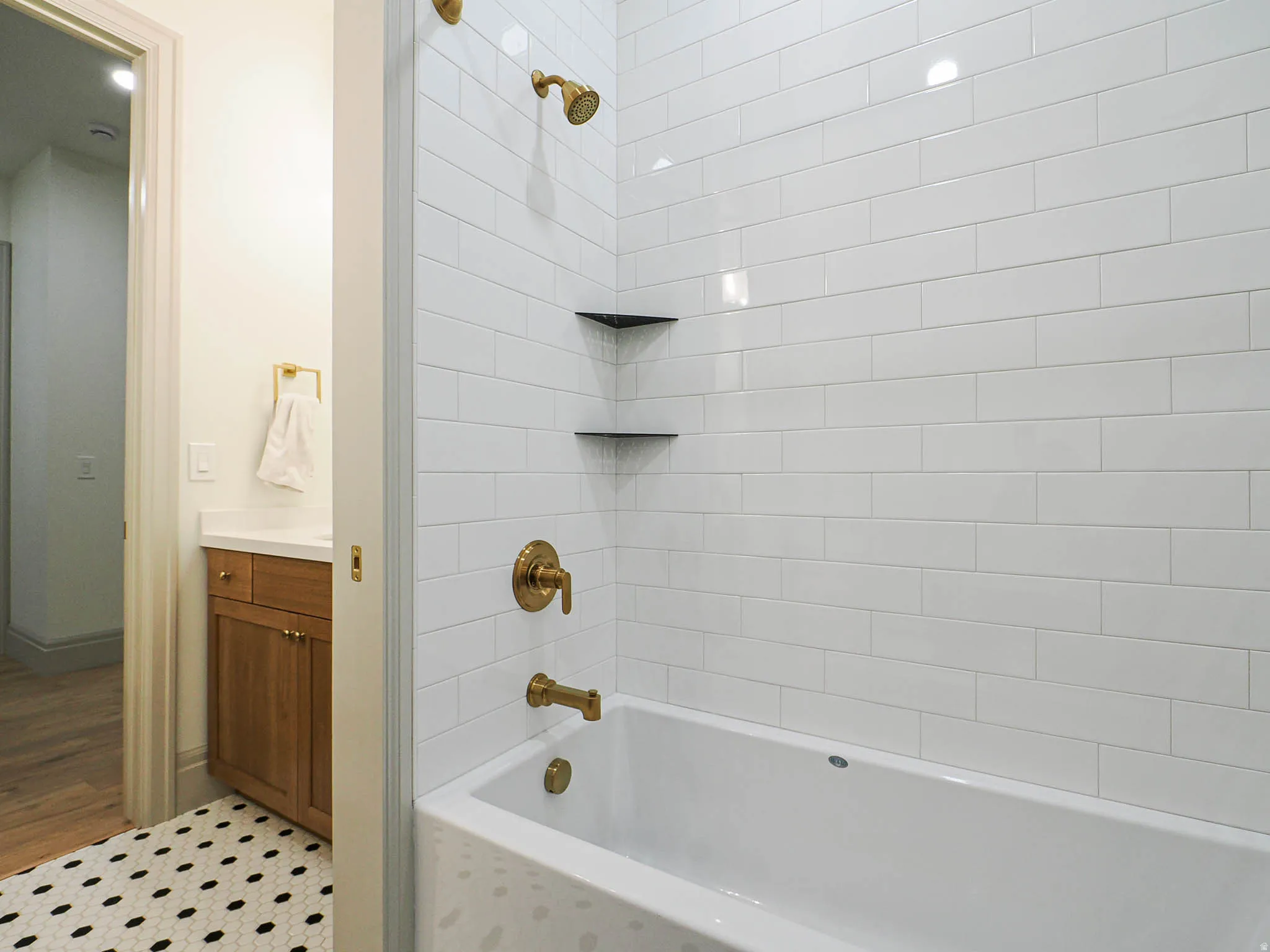 Bathroom featuring a white subway tile tub surround, bronze-finish plumbing fixtures, and two built-in corner shelves