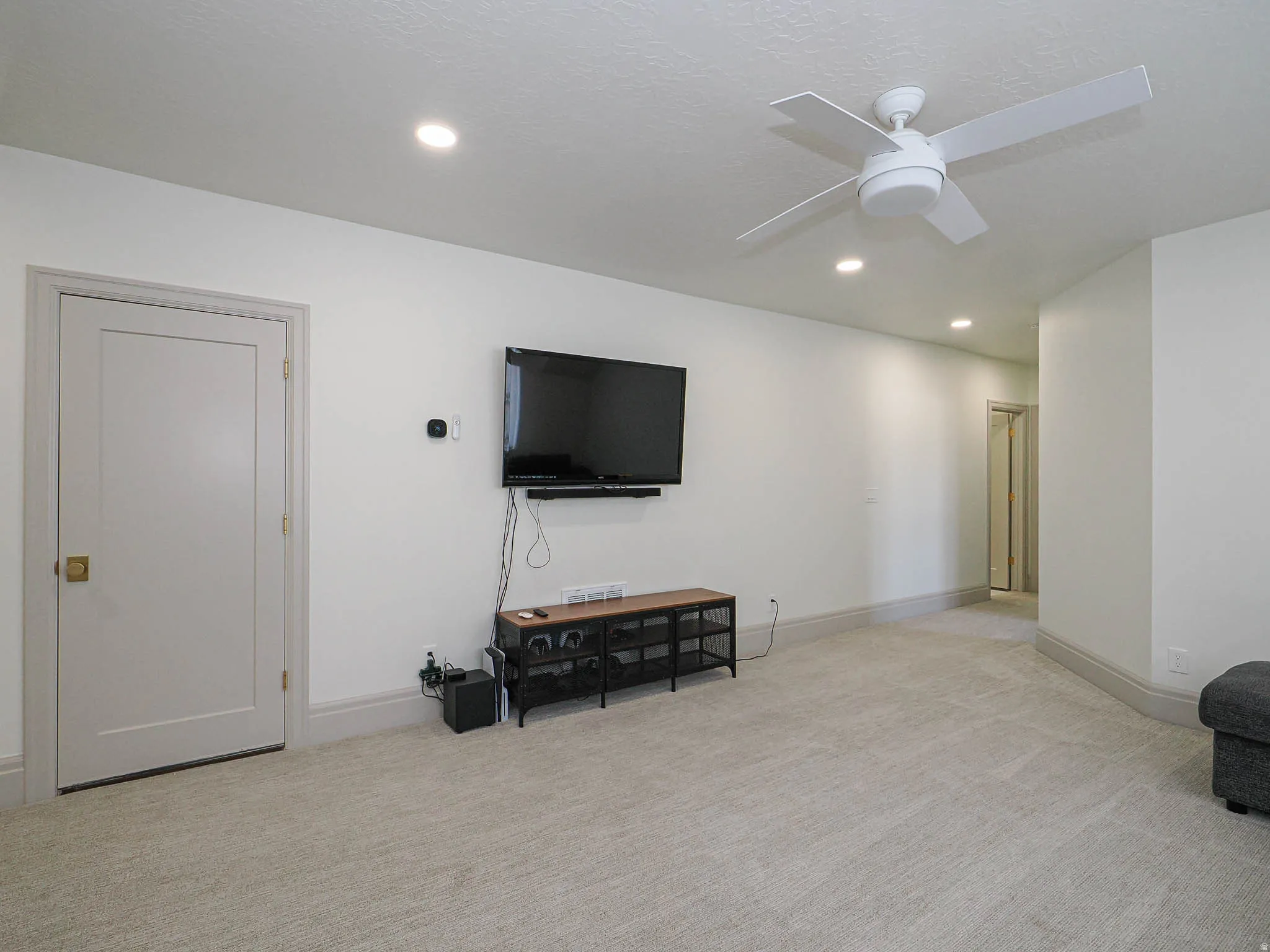 Neutral tone carpeted room featuring a white ceiling fan and recessed lighting