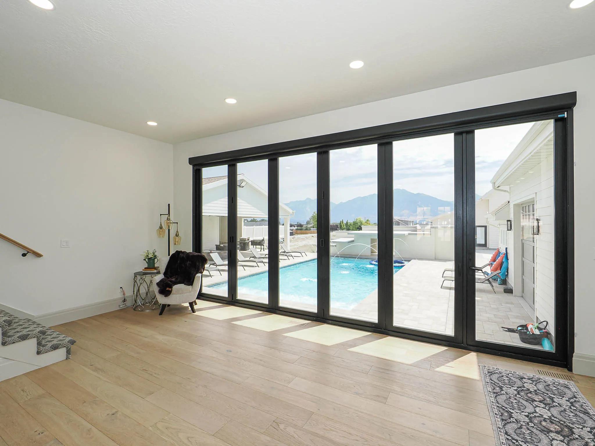 Expansive folding glass doors providing access to a stone-paved patio and swimming pool with water features