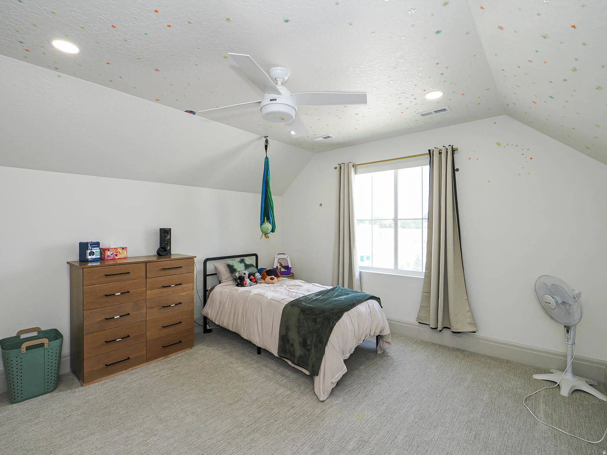 Attic room featuring an angled ceiling with recessed lighting, a ceiling fan, and a single window with curtain rod