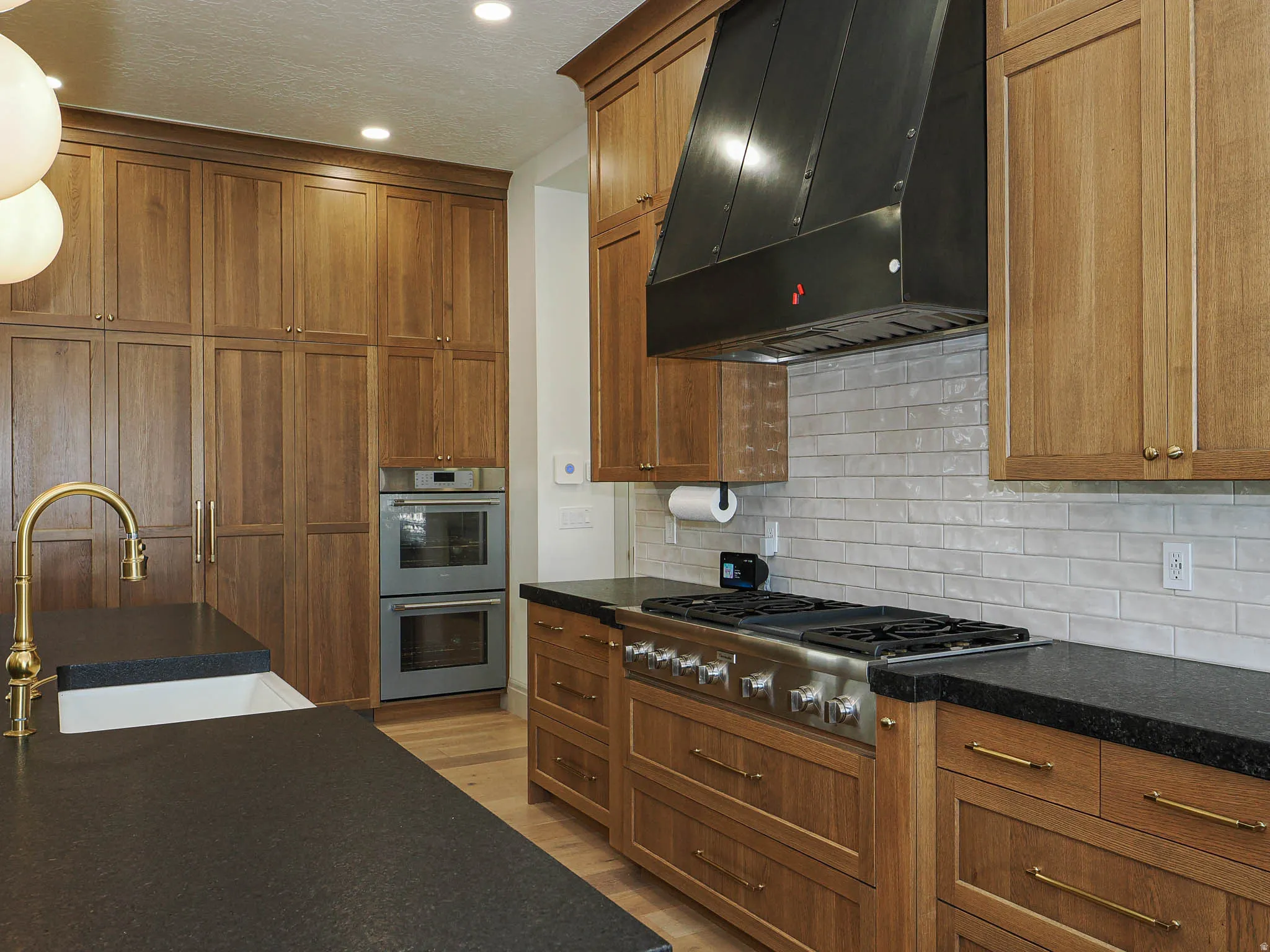 Gourmet kitchen featuring extensive wood cabinetry, stainless steel double wall ovens, a large professional-grade range with a custom range hood, and dark countertops