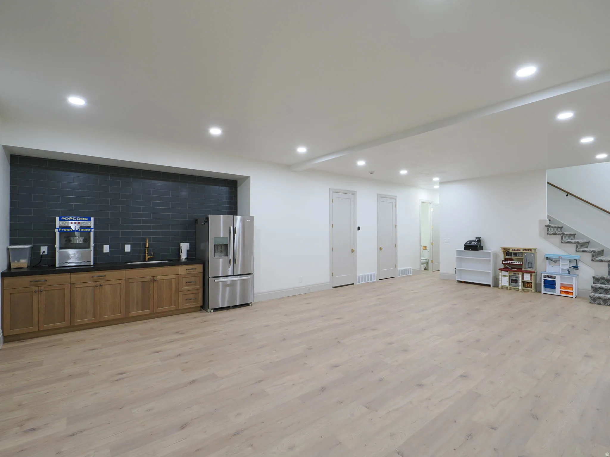 Spacious room featuring light wood-finish flooring, recessed lighting, and a built-in wet bar