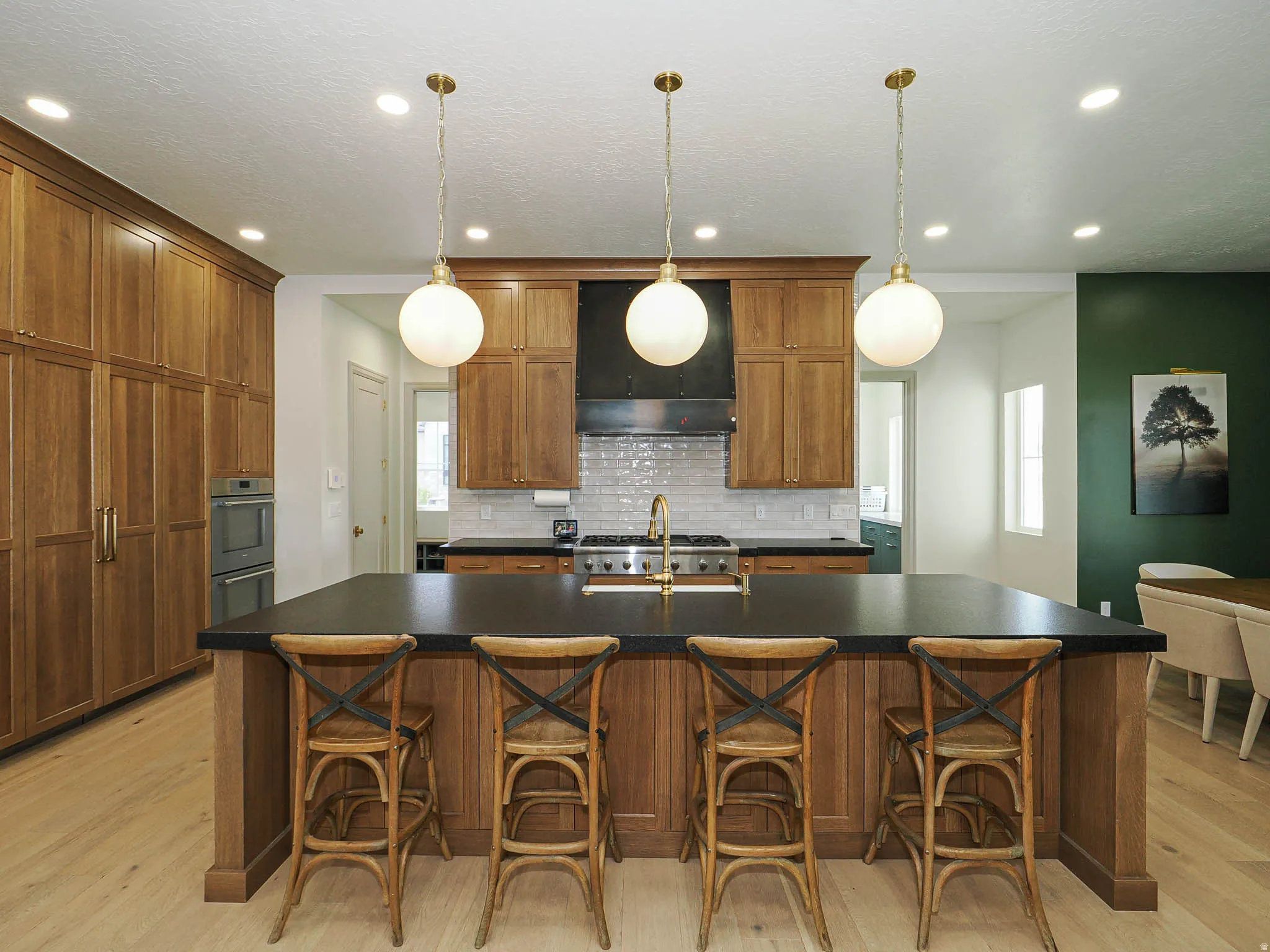 Spacious kitchen featuring a large central island with seating, a professional-grade range, custom wood cabinetry, stainless steel double ovens, and light wood-finish flooring