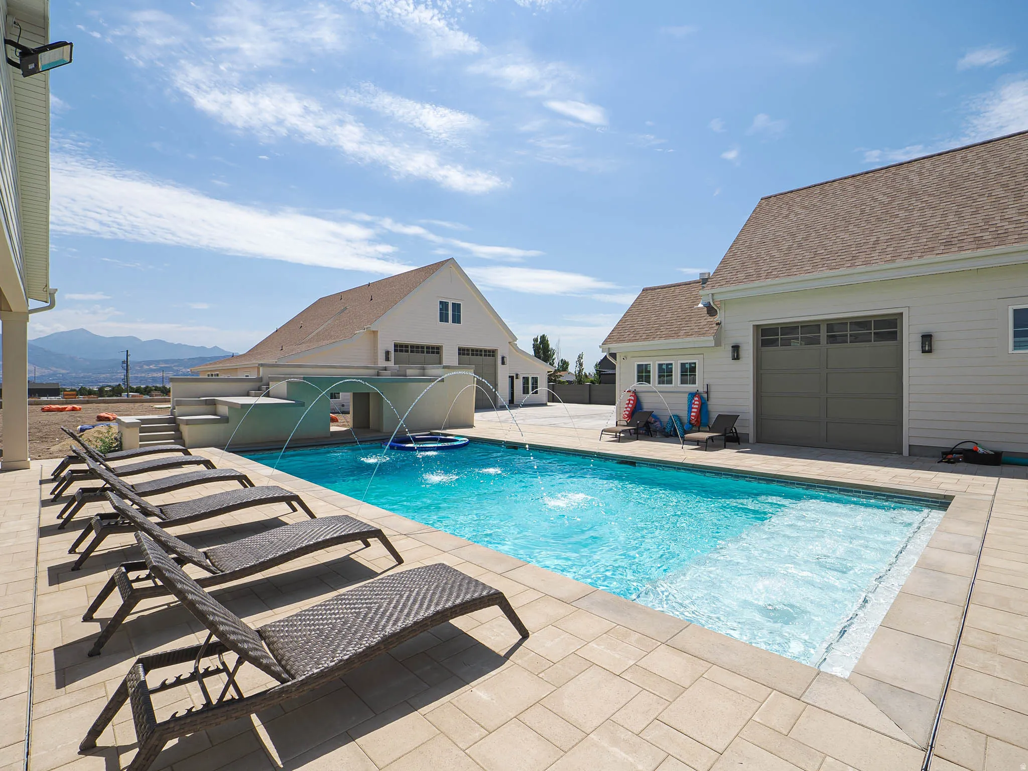 Private outdoor swimming pool with water features, paver patio, and adjacent structures