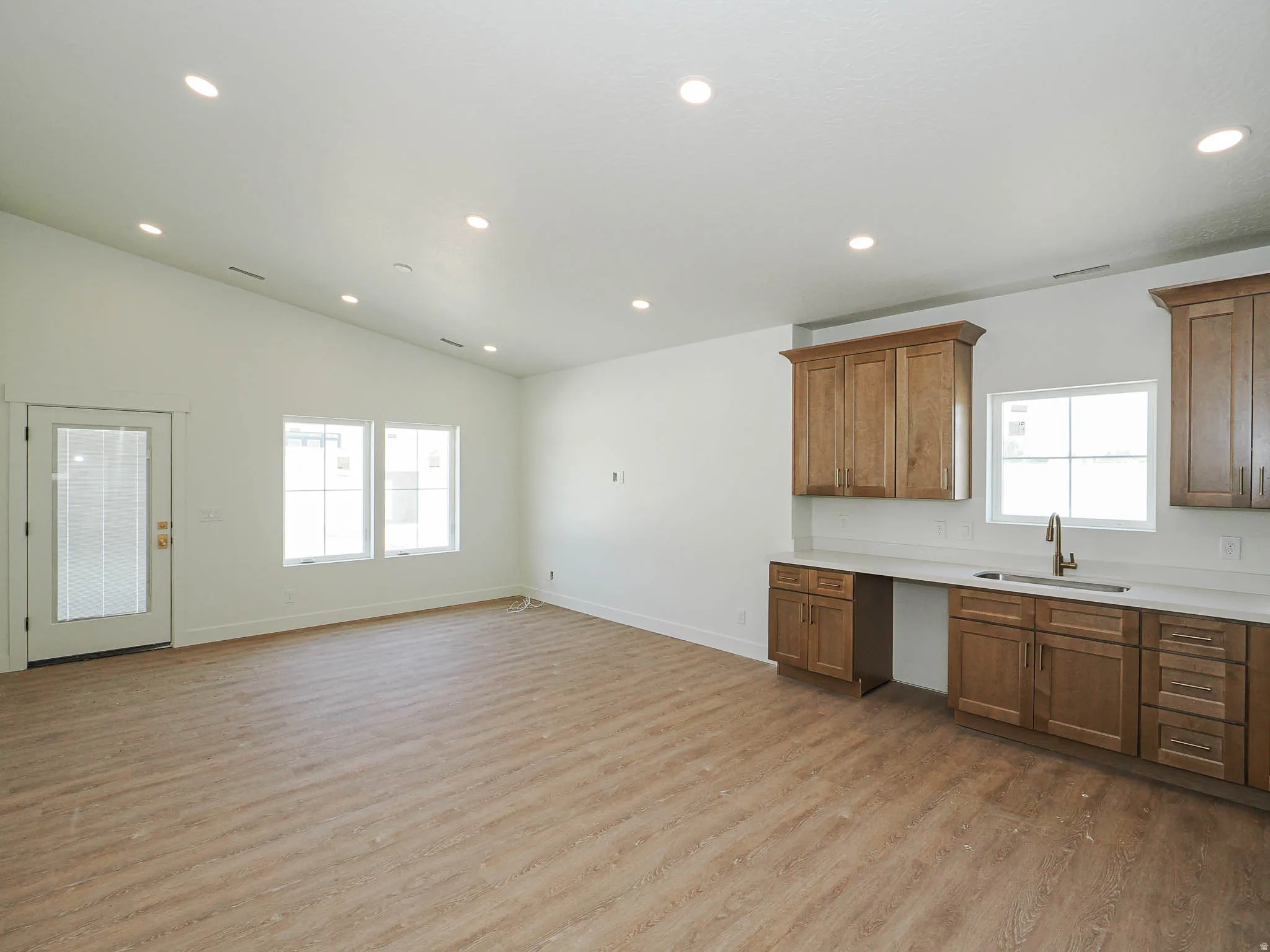 Vaulted ceilings highlight this open-concept space featuring wood-finish flooring, recessed lighting, and a built-in wet bar with a sink, cabinetry, and light-toned countertops