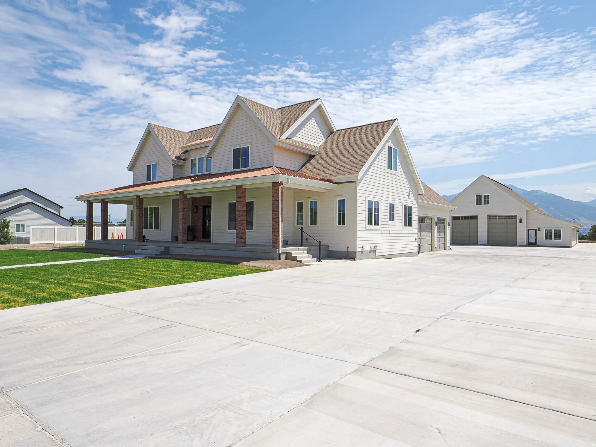 Contemporary farmhouse exterior featuring white siding, a covered front porch with brick columns, a three-car garage, and a separate detached garage structure