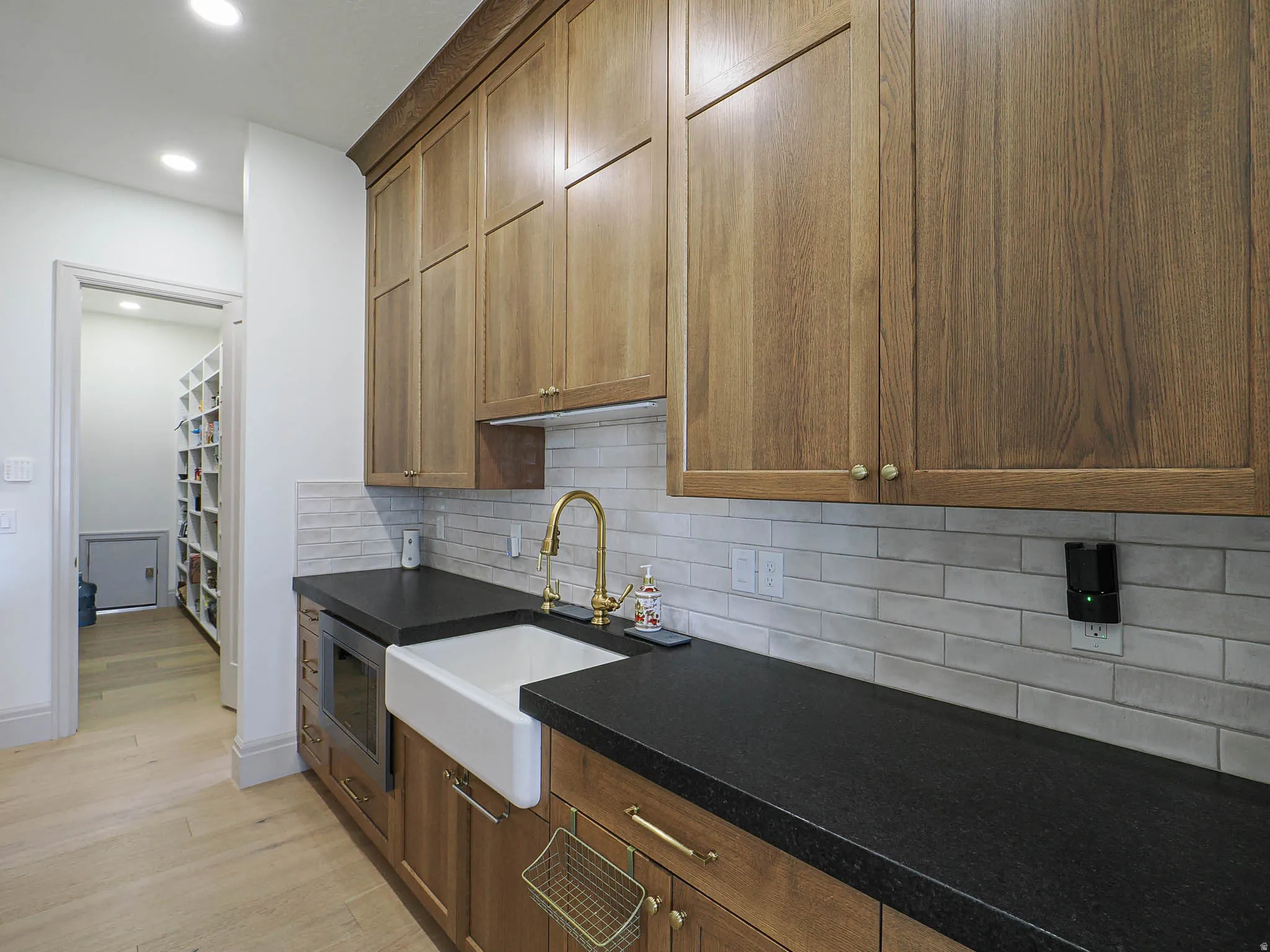 Functional utility space featuring wood-finish cabinetry, dark countertops, and a white farmhouse-style sink with a brass-finish faucet