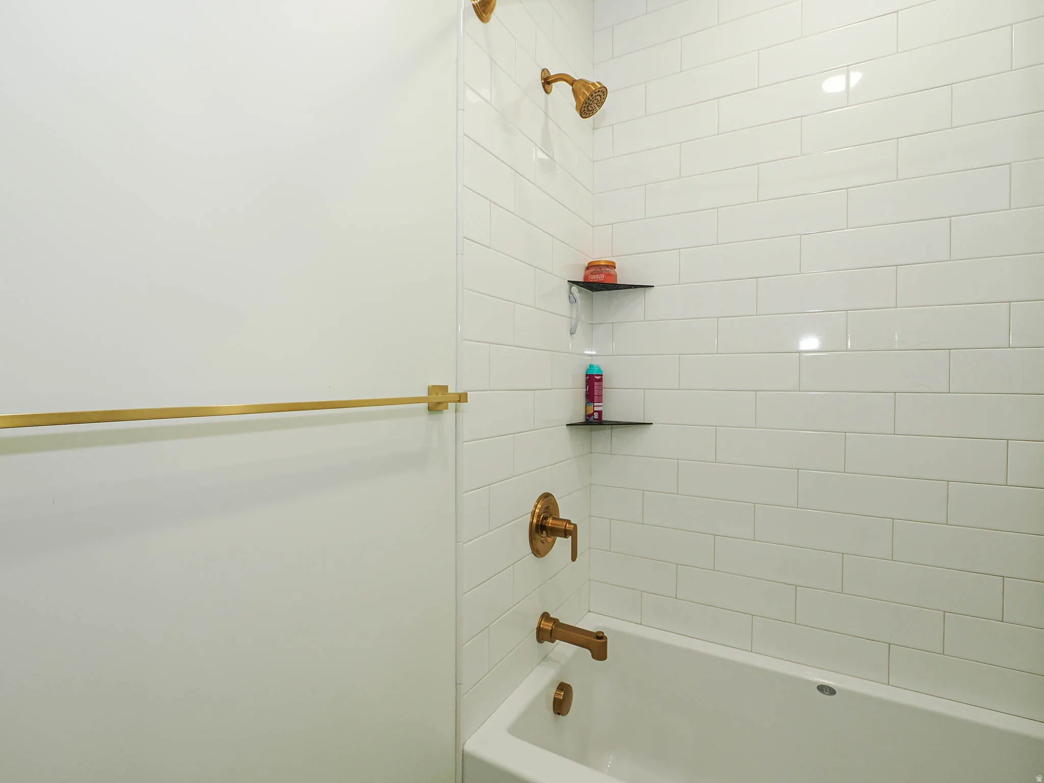 White subway tile shower surround with integrated corner shelving, gold-tone shower head, and matching tub filler