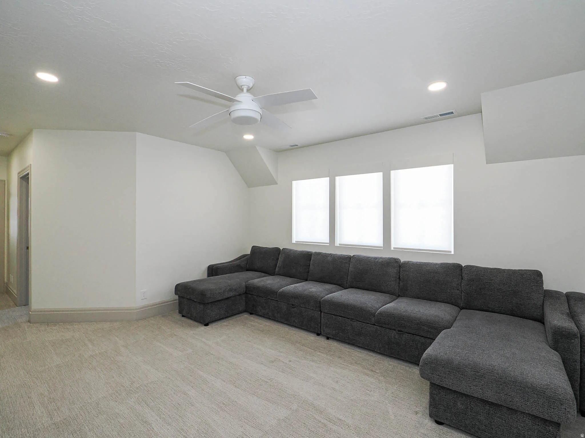 Spacious room featuring light-colored carpeting, three windows with blinds, recessed lighting, and a ceiling fan