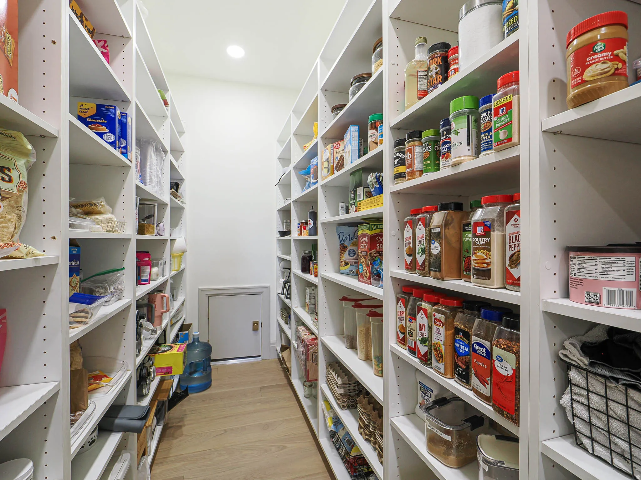 Walk-in pantry featuring extensive white shelving, wood-finish flooring, recessed lighting, and a white access door