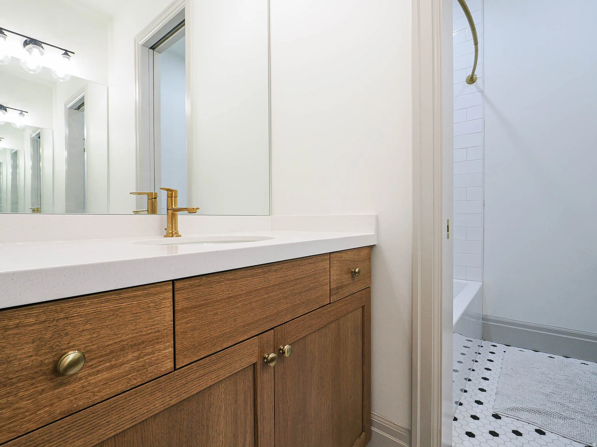 Wood-finish vanity with brass hardware, a white countertop, and a contemporary brass faucet