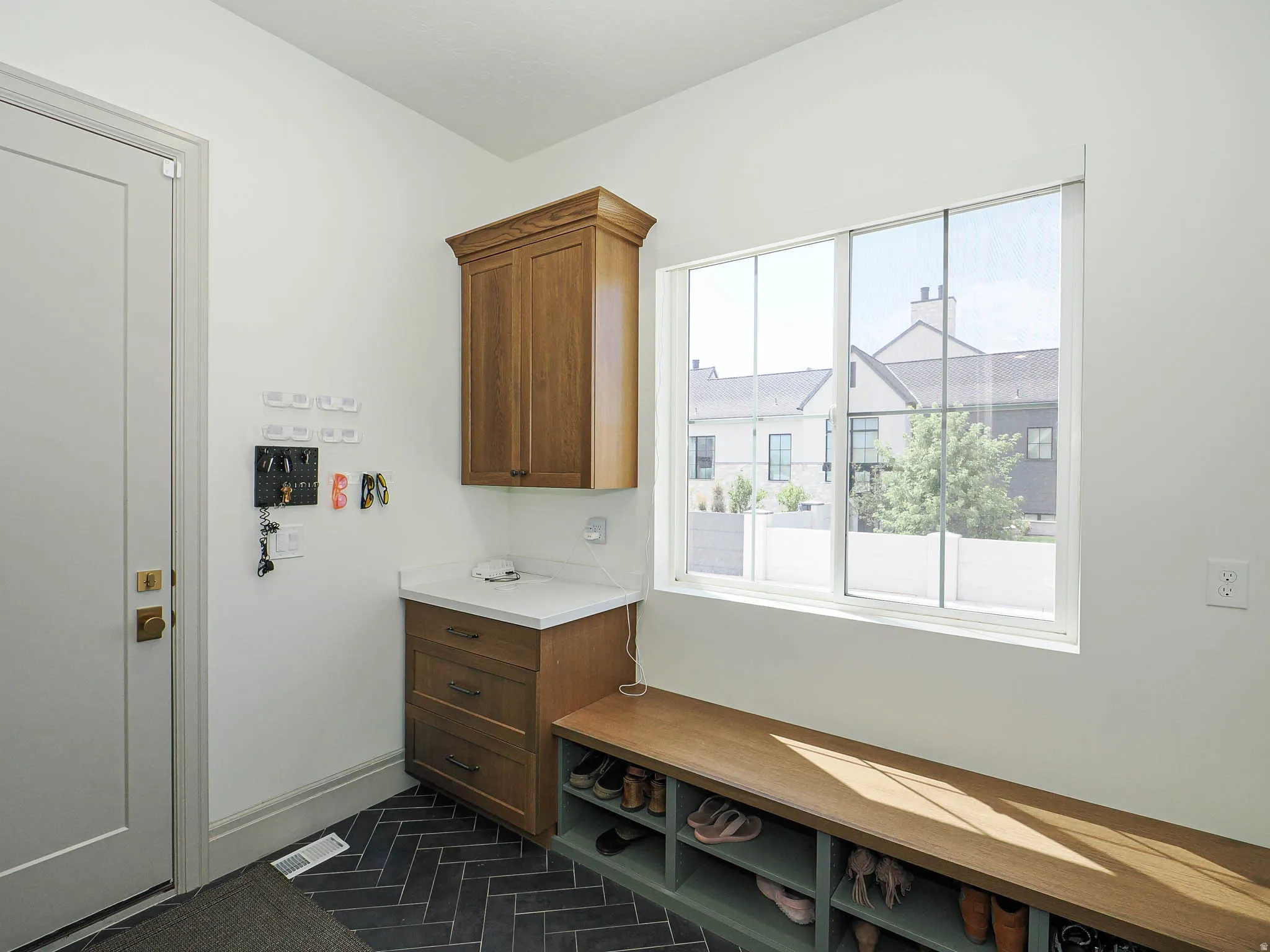 Entryway featuring herringbone tile flooring, built-in wooden cabinetry with a countertop, an integrated wooden bench with shoe storage, and a large window providing natural light