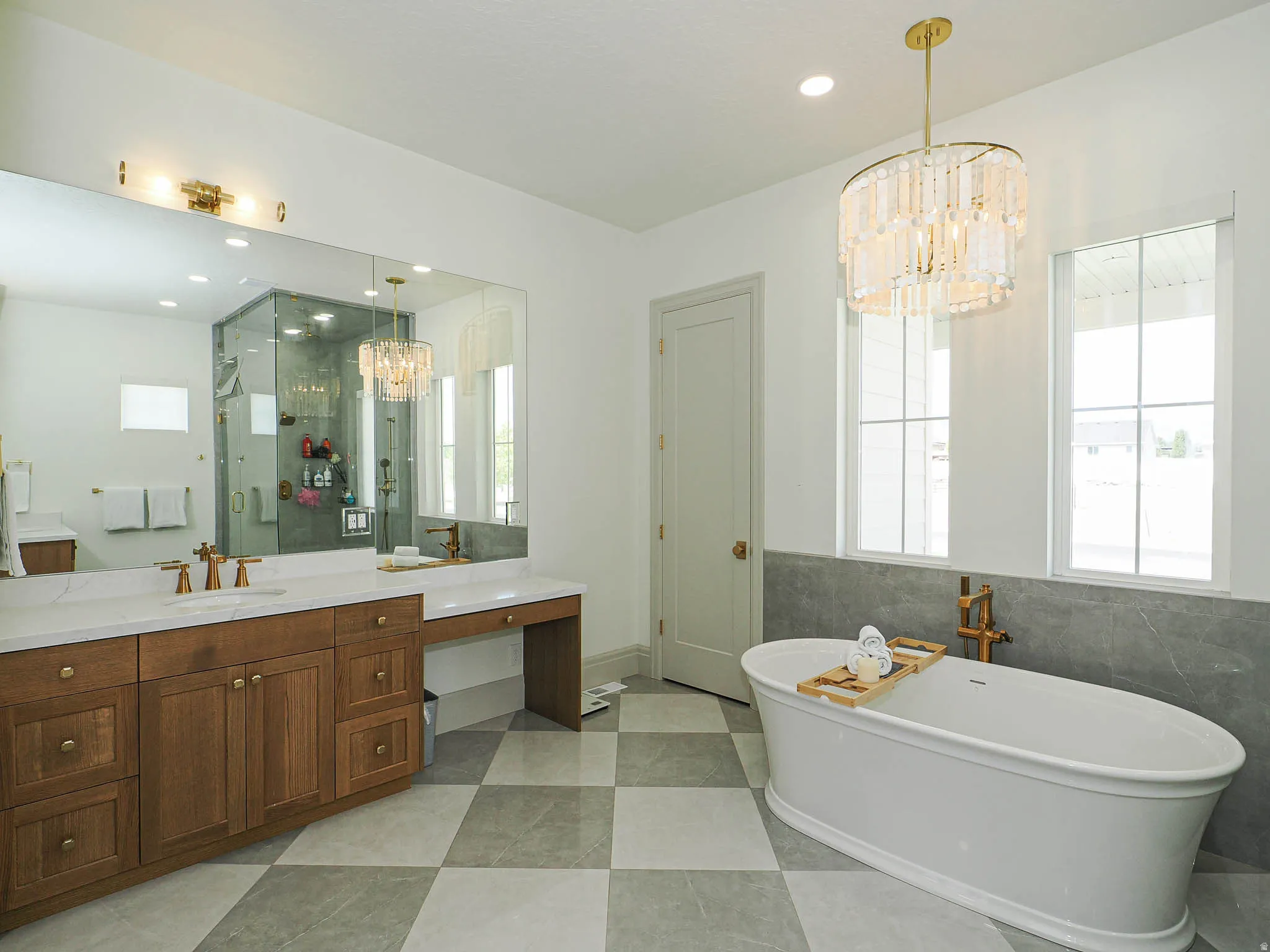 Freestanding soaking tub with floor-mounted fixture, checkered tile flooring, and a large vanity with dual sinks