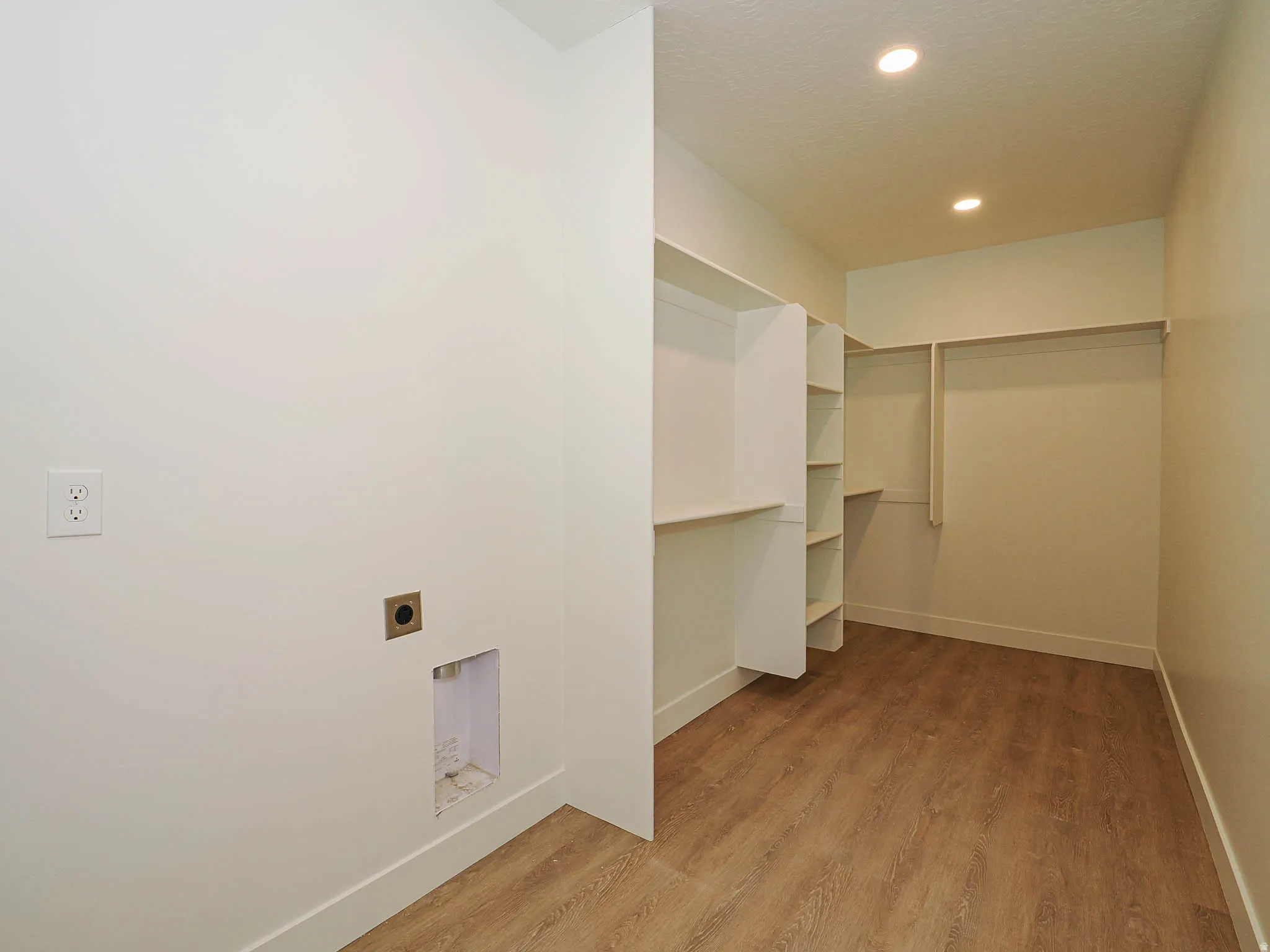 Laundry area featuring wood-finish flooring, recessed lighting, and integrated shelving with hanging rods