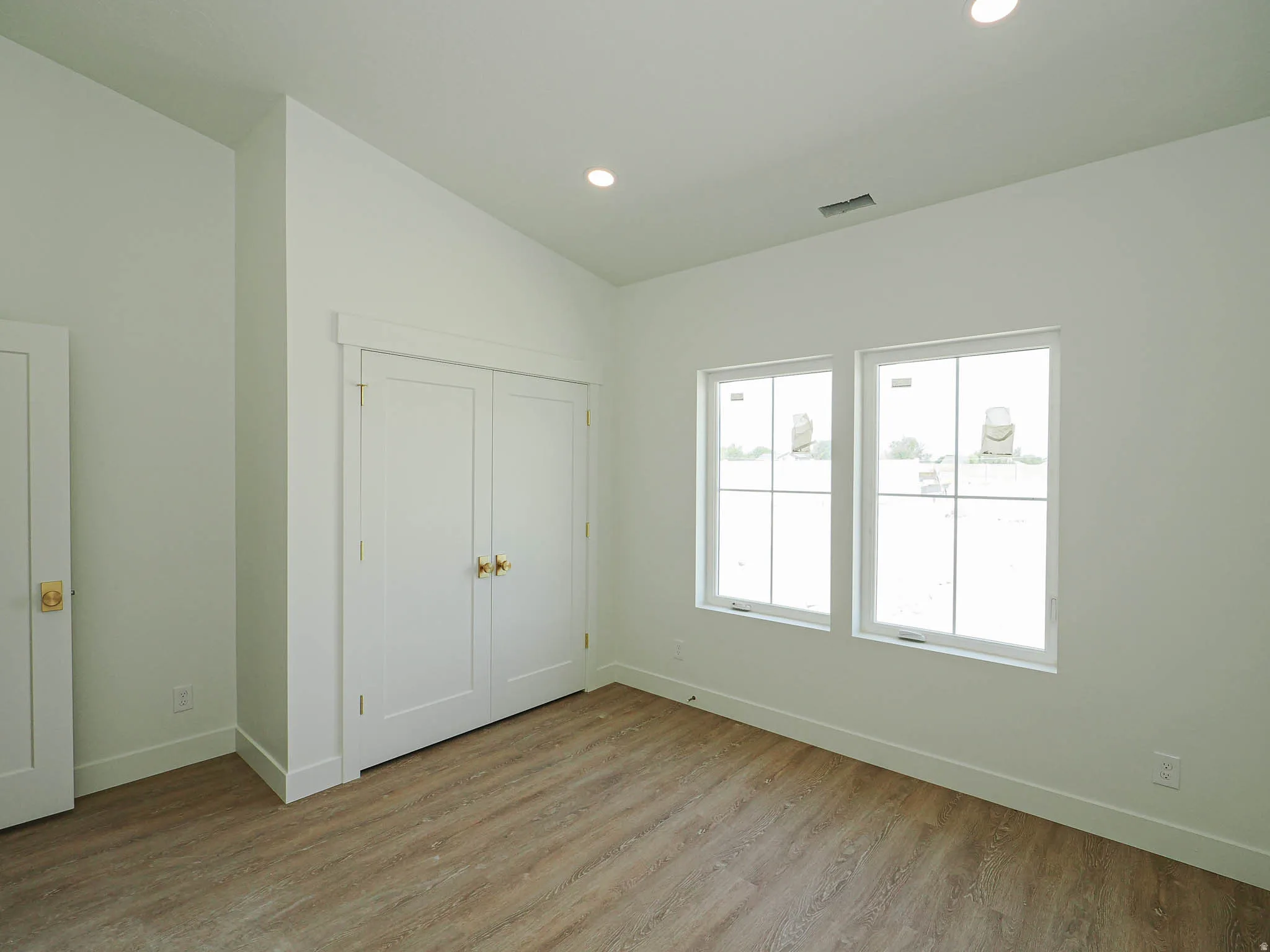 Room featuring two white-framed windows, a double-door closet with brass hardware, and wood-finish flooring