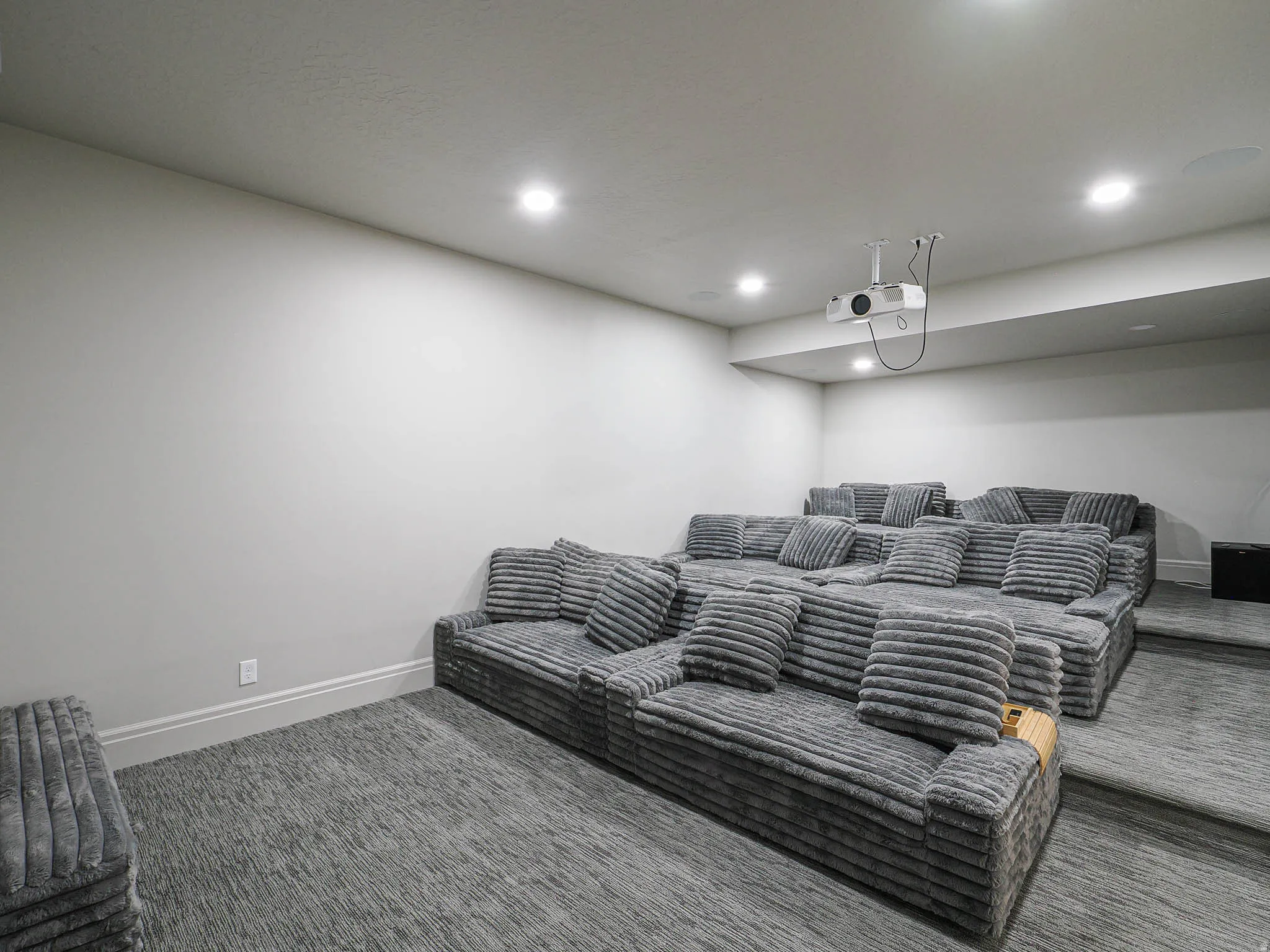 Dedicated media room featuring tiered seating, recessed lighting, ceiling-mounted projector, and wall-to-wall carpeting