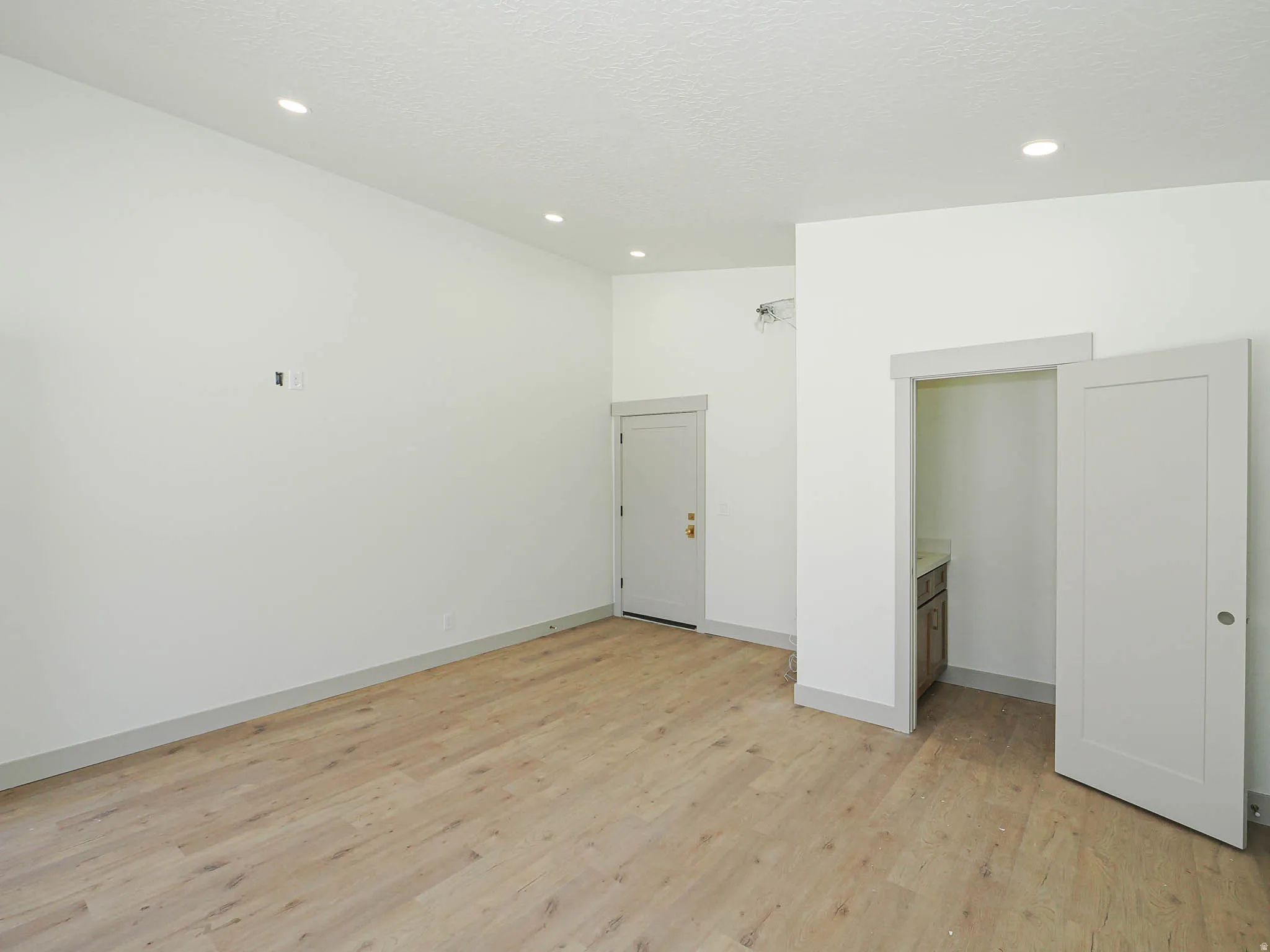 Open room featuring light wood-finish flooring, recessed ceiling lighting, and crisp white walls