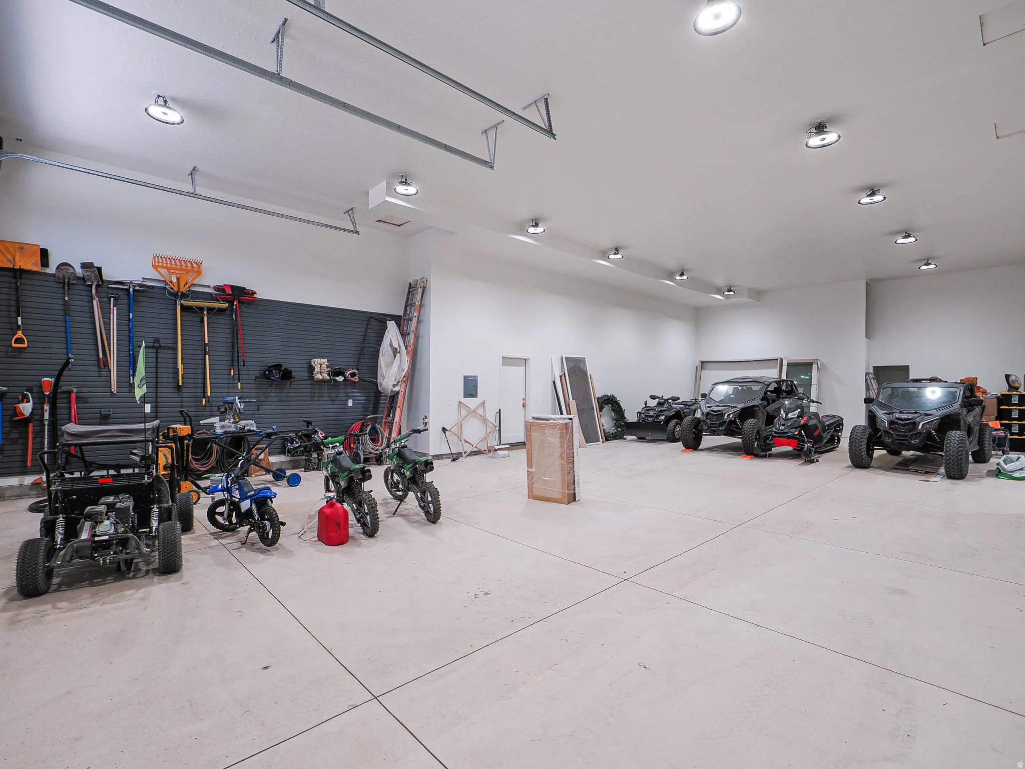 Expansive garage with high ceilings, multiple flush-mount ceiling lights, light-colored concrete flooring, and a comprehensive slatwall organization system for tools