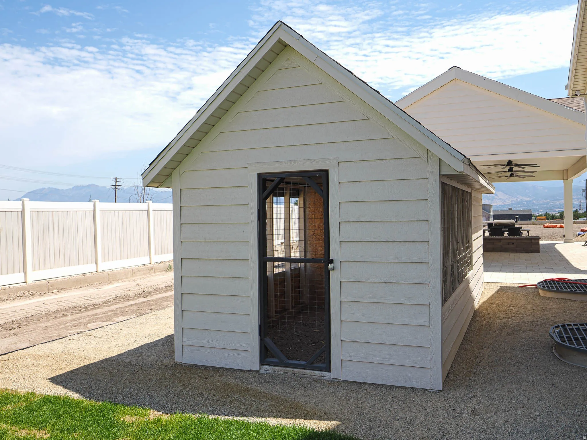Detached storage shed with white horizontal siding and a black screen door