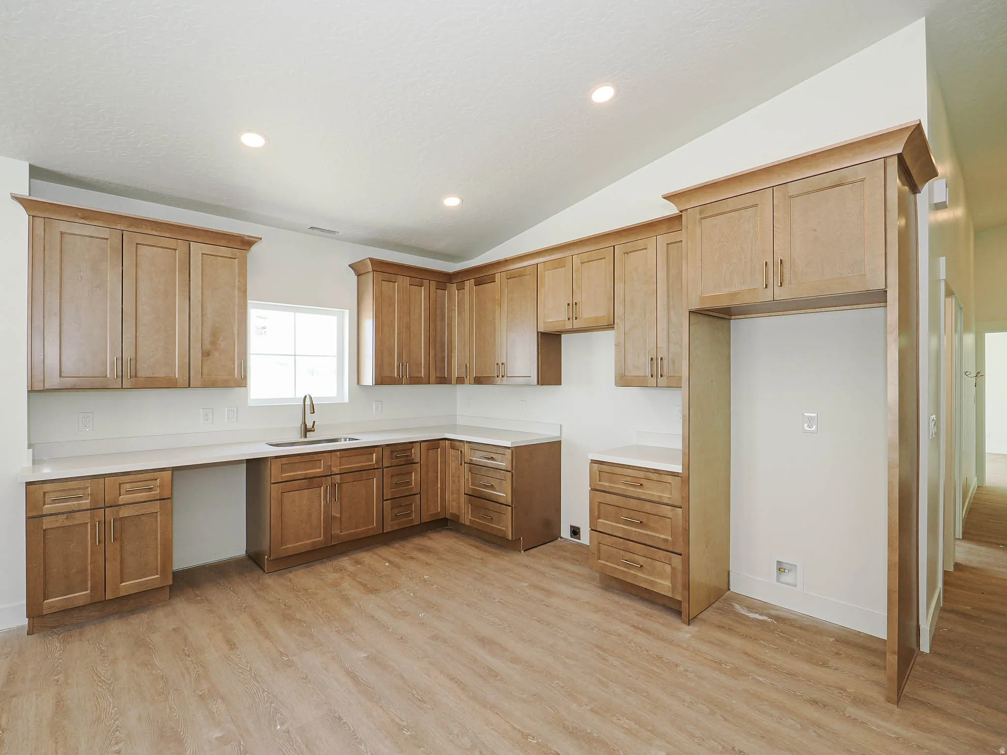Open-concept kitchen featuring light wood-finish cabinetry, white countertops, a white subway tile backsplash, and wood-finish flooring