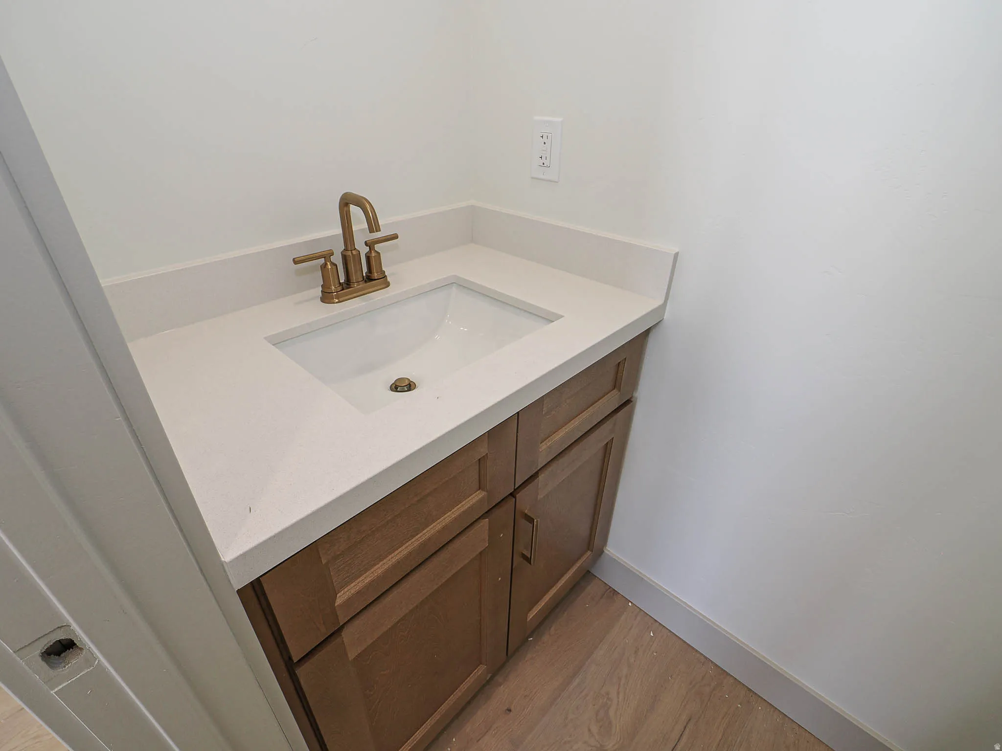 Vanity featuring a light countertop with an integrated sink, a bronze-finish faucet, and wood-finish cabinetry with bronze hardware