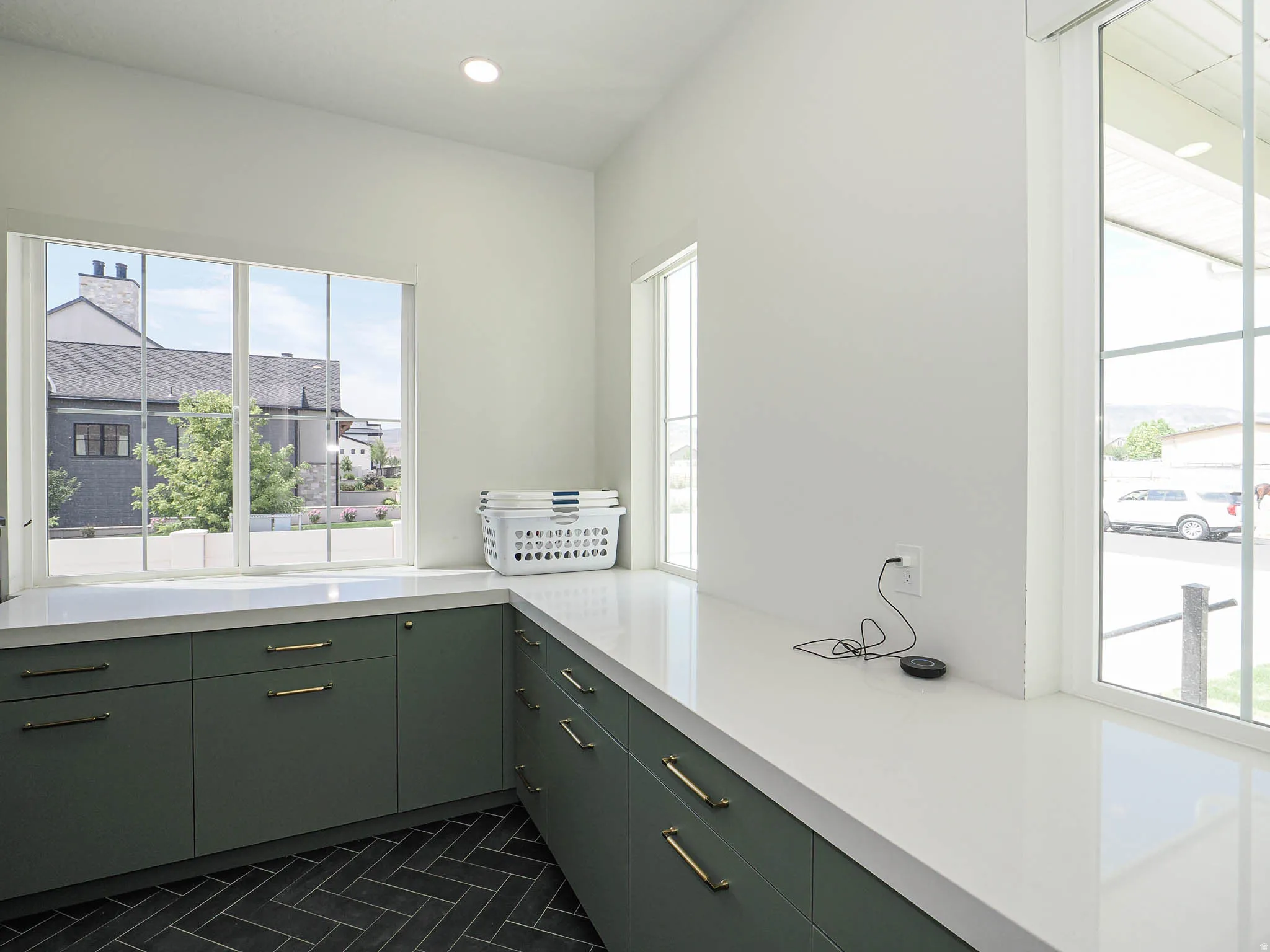 Spacious utility area featuring dark green cabinetry with brass hardware, white countertops, and a dark herringbone tile floor