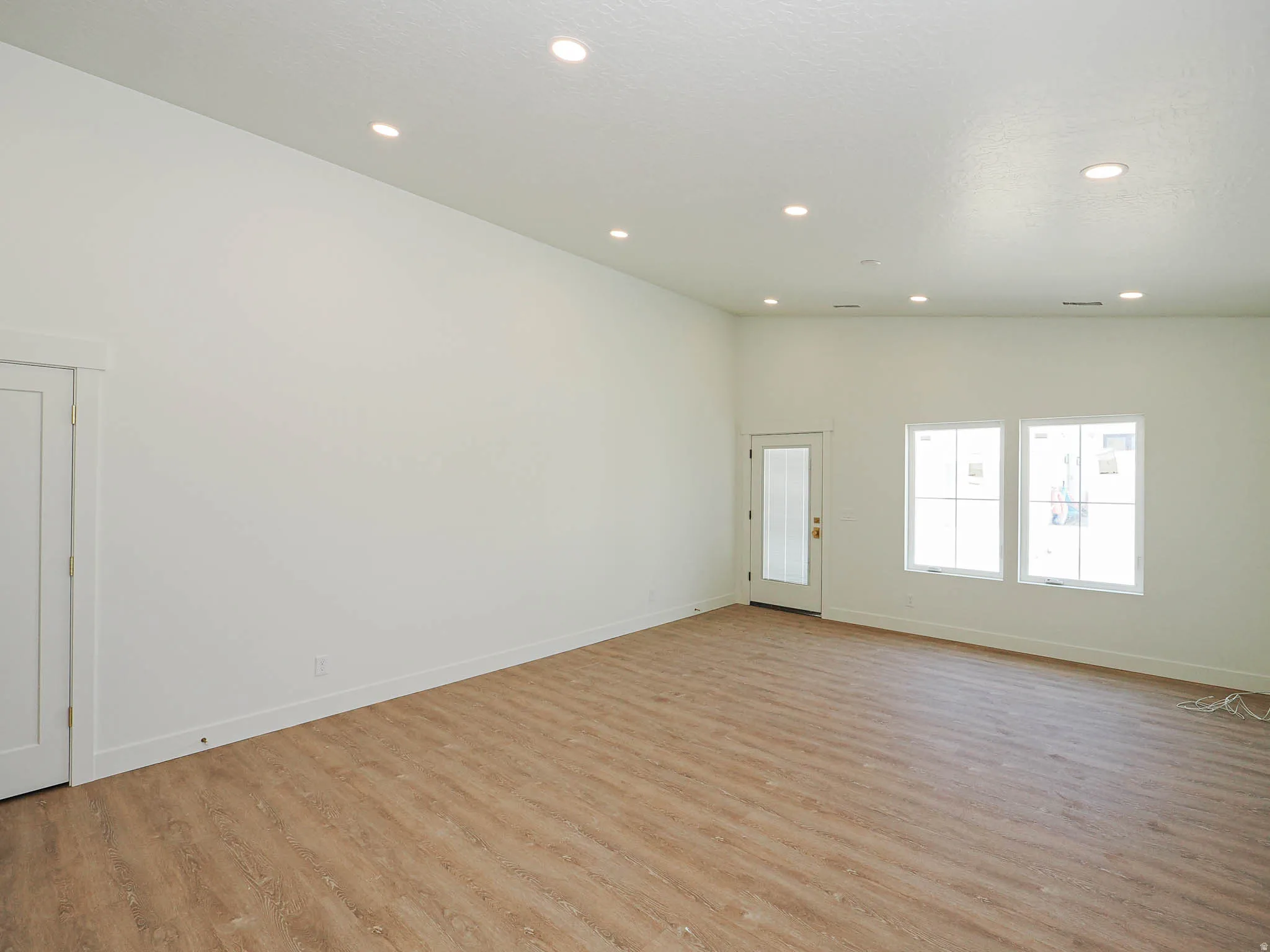 Spacious room featuring wood-finish flooring, recessed lighting, and white baseboards