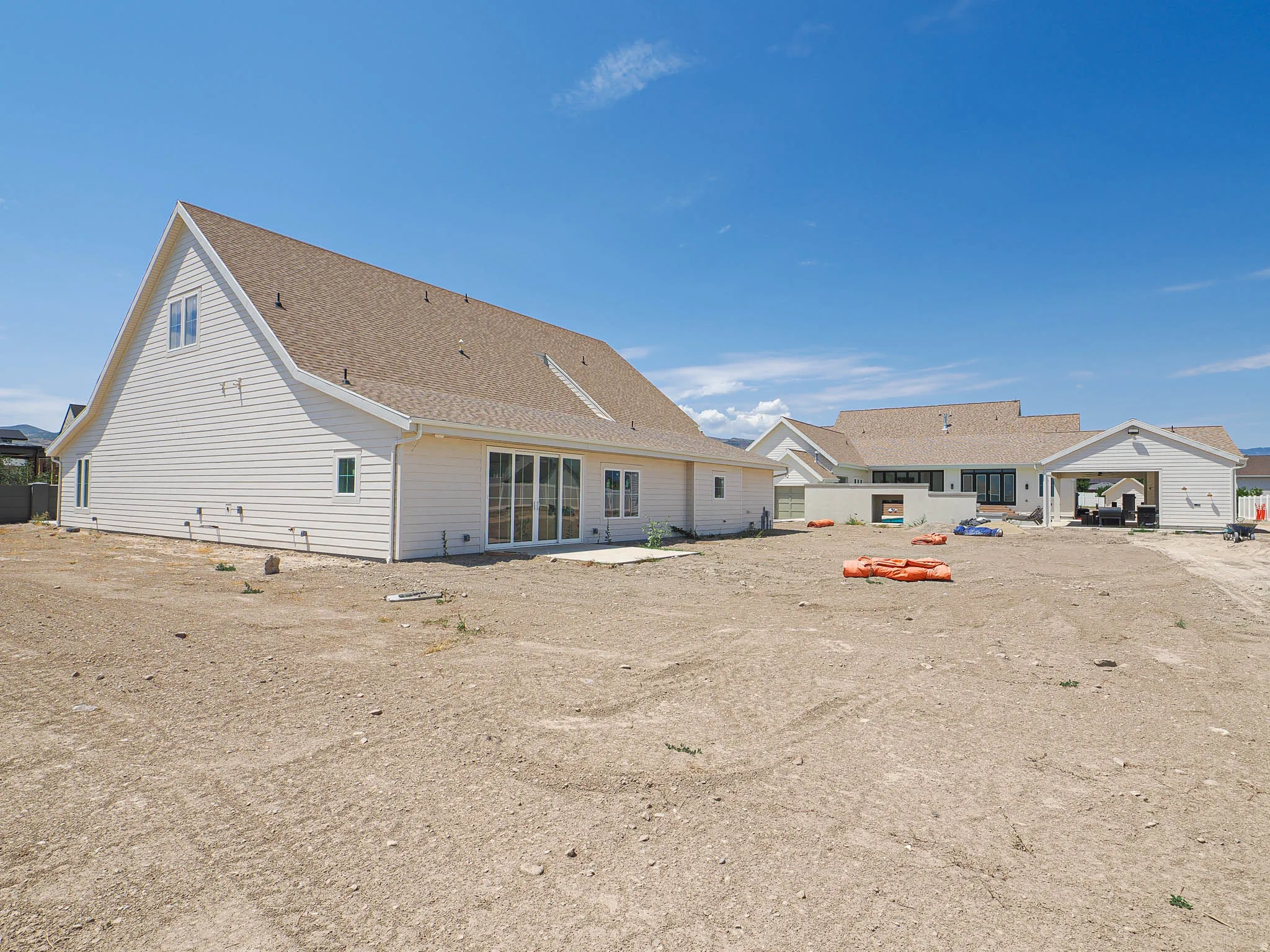 White siding exterior with a brown shingle roof, featuring multiple large sliding glass doors, a rear patio, and an attached garage structure