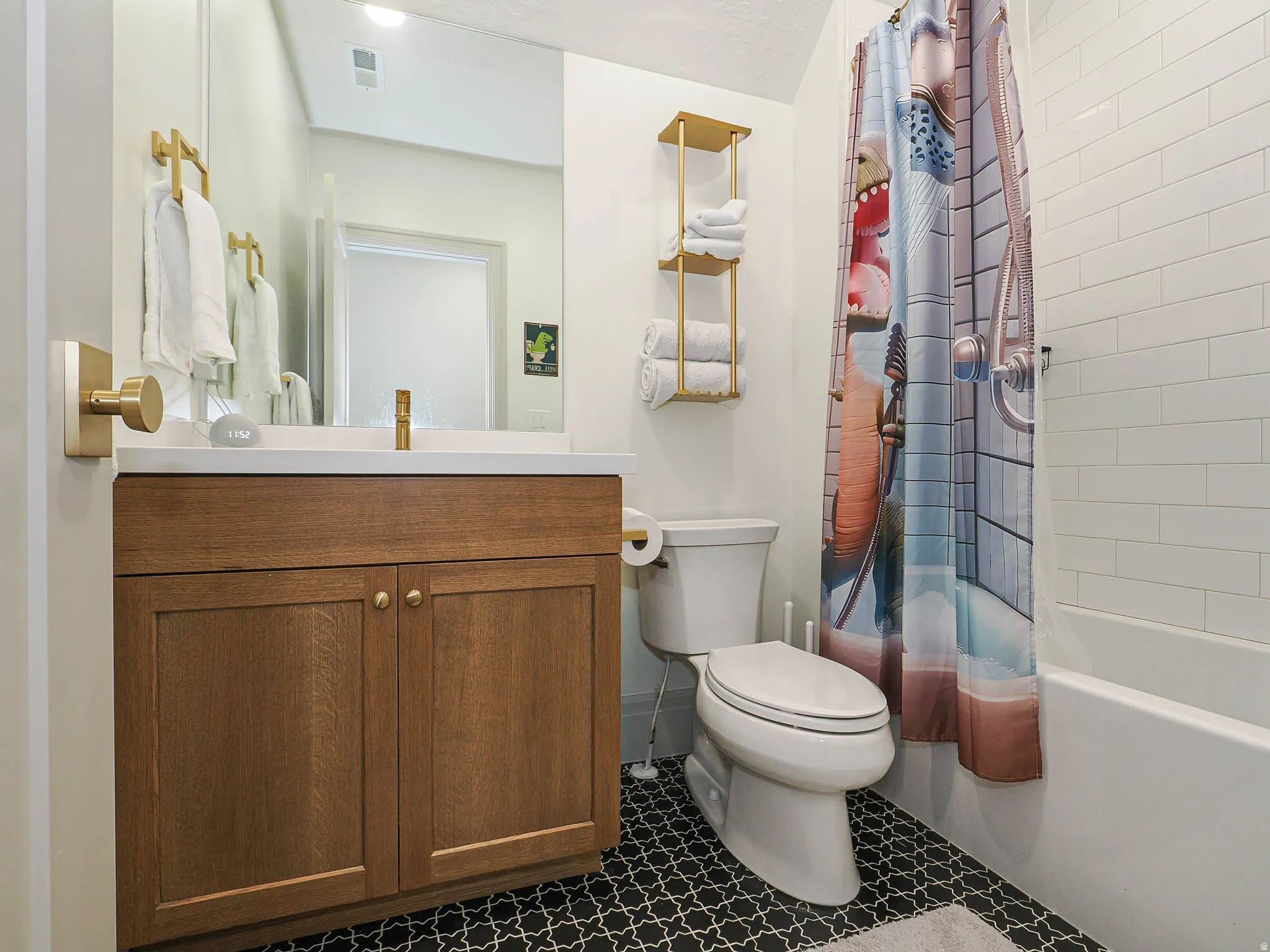 Bathroom featuring a wood-finish vanity with an integrated sink, black and white patterned floor tile, white subway tile shower surround, and a chrome shower fixture
