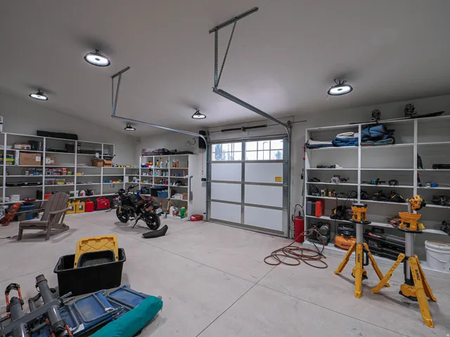 Concrete-floor garage with multiple built-in shelving units, overhead lighting, and an overhead door with frosted glass panels