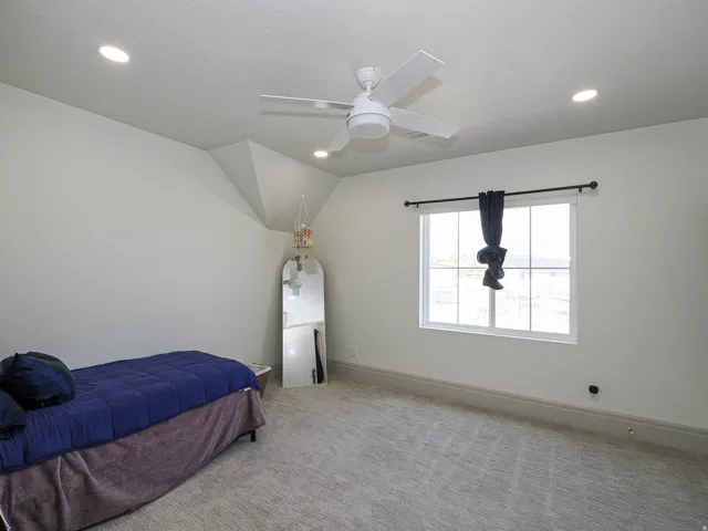 Carpeted room featuring a white ceiling fan, recessed lighting, a window with grid patterns, and substantial baseboards