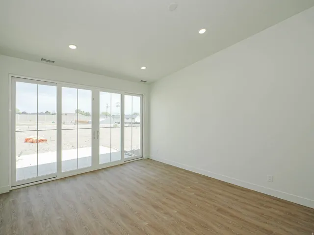 Expansive sliding glass doors, wood-finish flooring, recessed lighting, white walls, and a visible patio area
