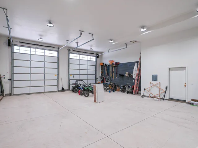 Spacious garage featuring two overhead doors with transom windows, exposed ceiling tracks, and ample overhead lighting