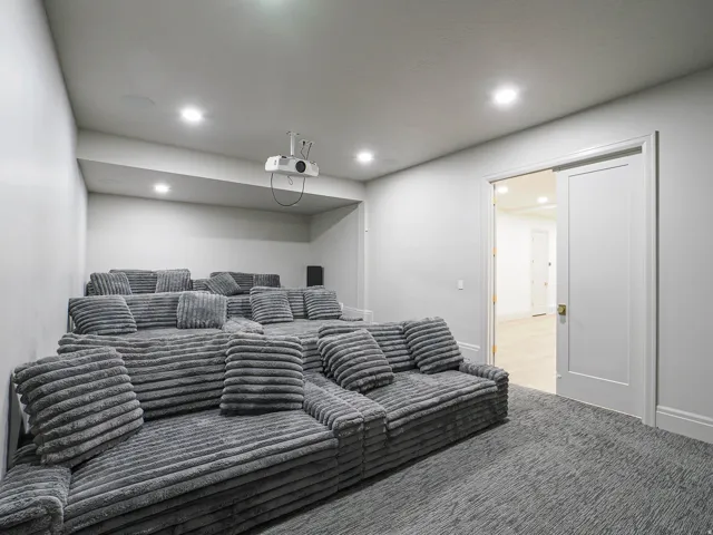 Dedicated media room featuring tiered seating, recessed lighting, a ceiling-mounted projector, and dark textured carpeting