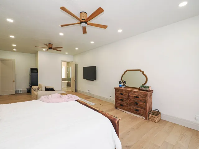 Spacious room featuring light wood-finish flooring, recessed lighting, and two ceiling fans with wood-look blades