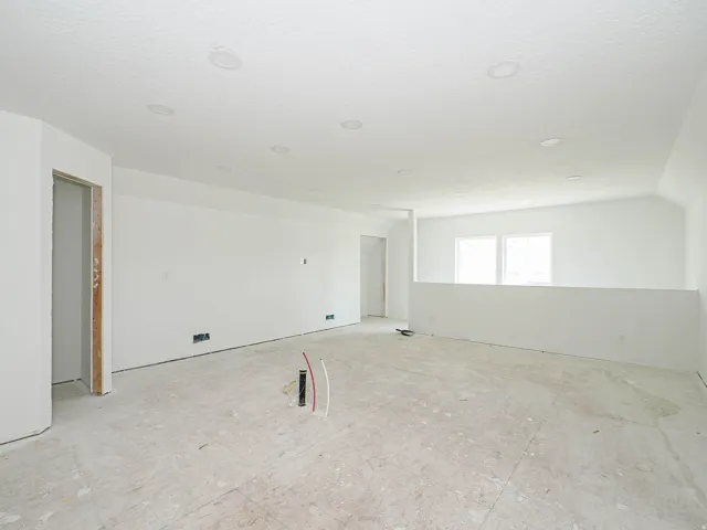 Expansive open-concept room featuring a half-wall partition, multiple recessed ceiling lights, and multiple windows providing natural light