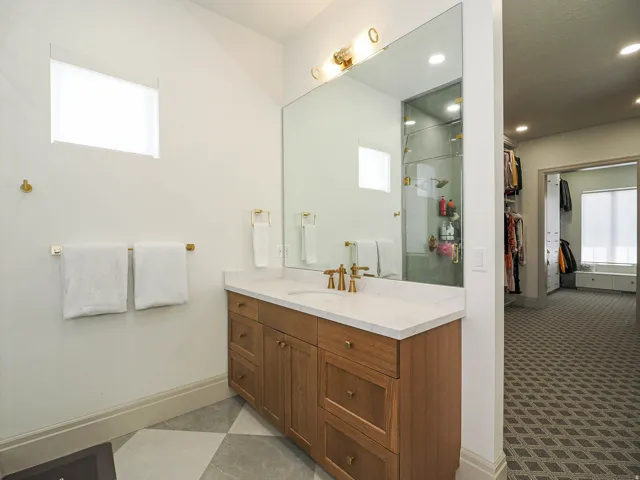 Bathroom vanity featuring a light wood-finish cabinet with brass hardware, a white countertop, and a large wall-mounted mirror