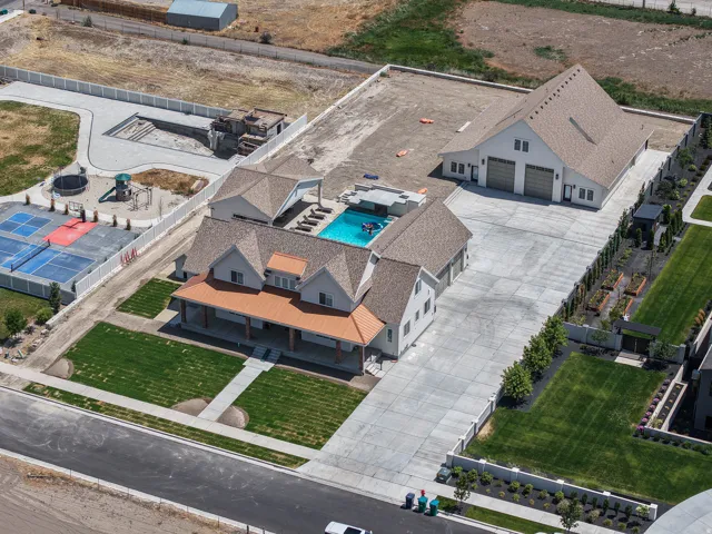 Expansive property featuring a large main residence with a covered front porch, a detached multi-car garage, a swimming pool with integrated lounge areas, a sports court, and a separate structure with an unfinished pool