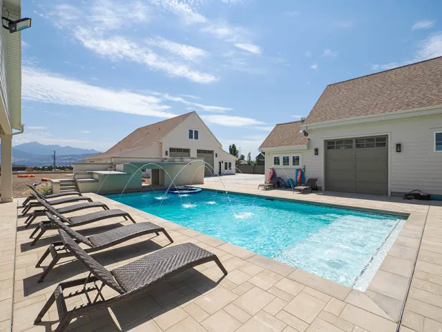 Private outdoor swimming pool with water features, paver patio, and adjacent structures
