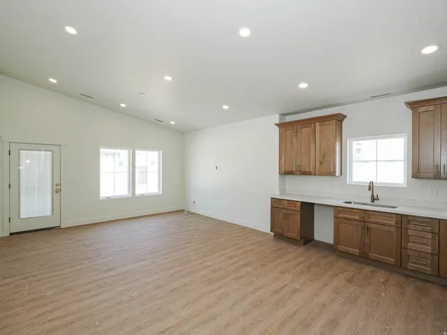 Vaulted ceilings highlight this open-concept space featuring wood-finish flooring, recessed lighting, and a built-in wet bar with a sink, cabinetry, and light-toned countertops
