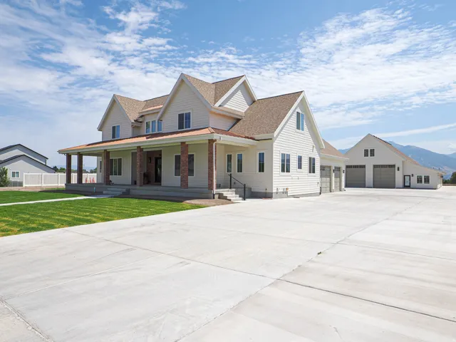 Contemporary farmhouse exterior featuring white siding, a covered front porch with brick columns, a three-car garage, and a separate detached garage structure
