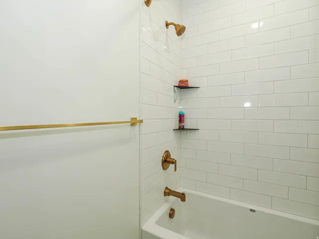 White subway tile shower surround with integrated corner shelving, gold-tone shower head, and matching tub filler