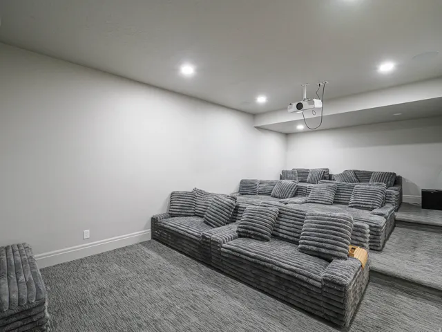 Dedicated media room featuring tiered seating, recessed lighting, ceiling-mounted projector, and wall-to-wall carpeting