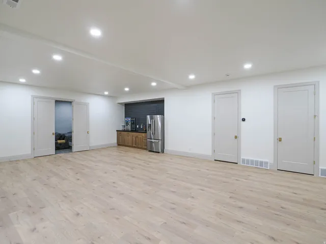 Spacious interior featuring wide plank wood-finish flooring, recessed lighting, and a built-in wet bar with a stainless steel refrigerator and dark tile backsplash