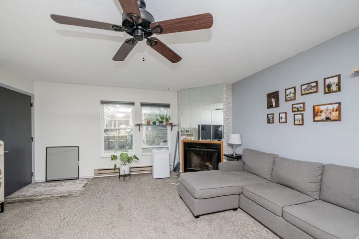 Living area with a ceiling fan, two windows, and a fireplace with mirror surround