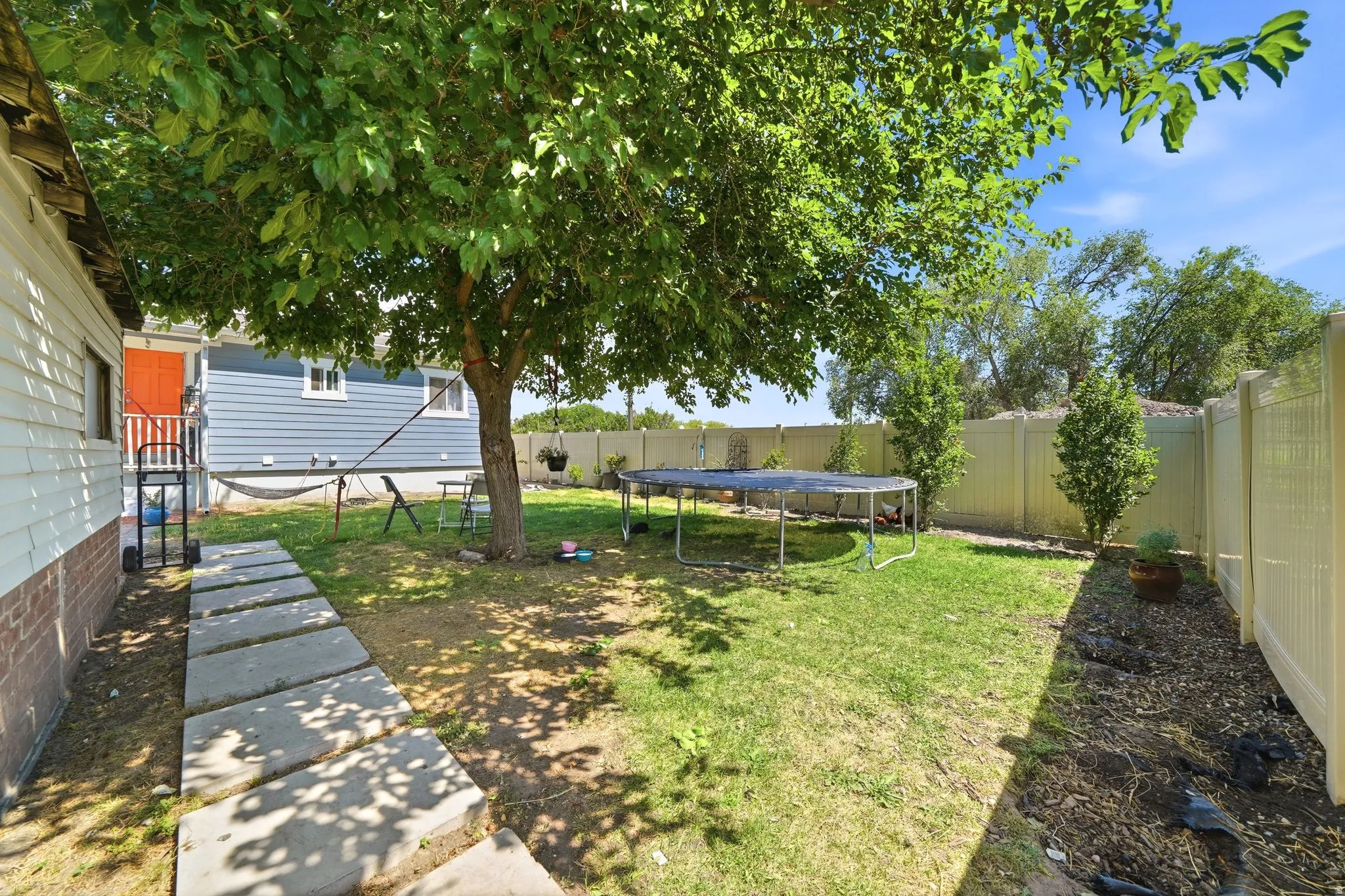 Spacious backyard featuring a substantial shade tree, concrete paver pathway, and perimeter fencing